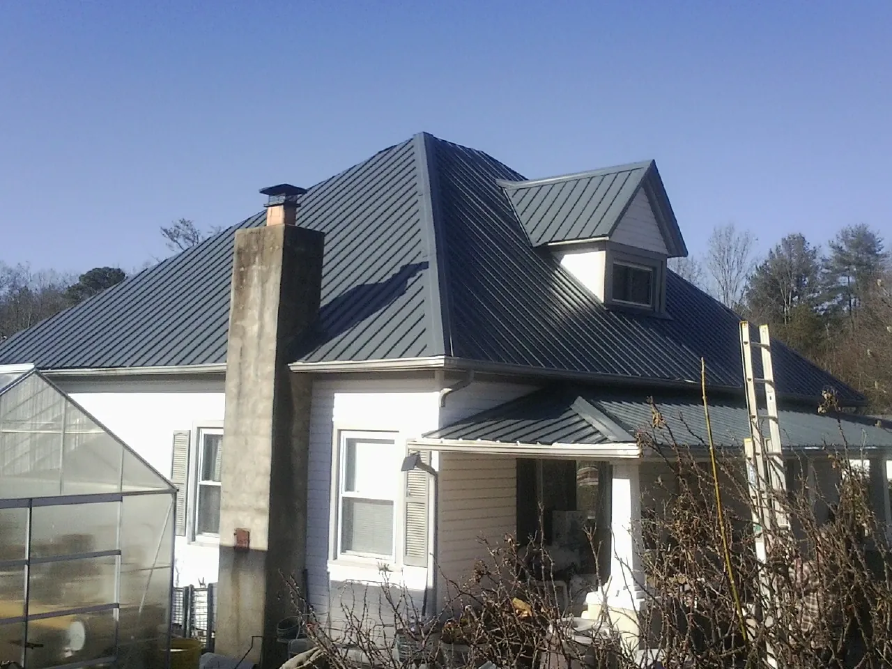Dark blue standing seam metal roof on a white farmhouse with dormer — Slate & Tile Roof Repair by Roofing Brothers in Spicer