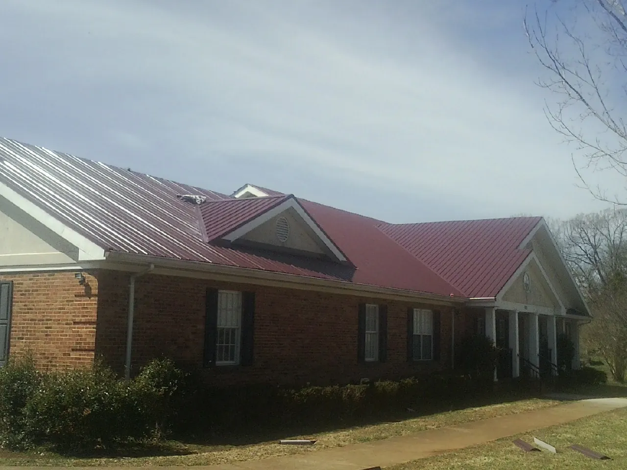 Red metal roof with gabled entries on a long brick building, from a Hail Damage Roof Repair job in Spicer