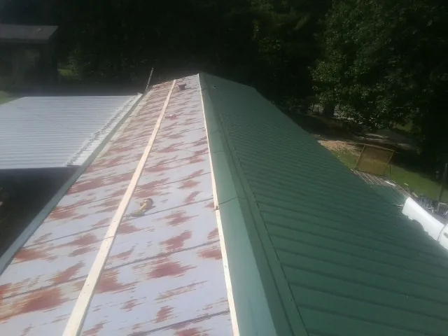 Old rusted panels beside newly installed green metal roofing — Wind Damage Roof Repair by Roofing Brothers in Spicer