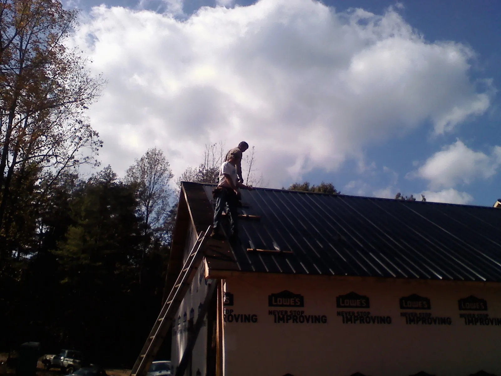 Roofer fastening dark metal panels high against a cloudy sky, from a Roof Inspection job in Spicer