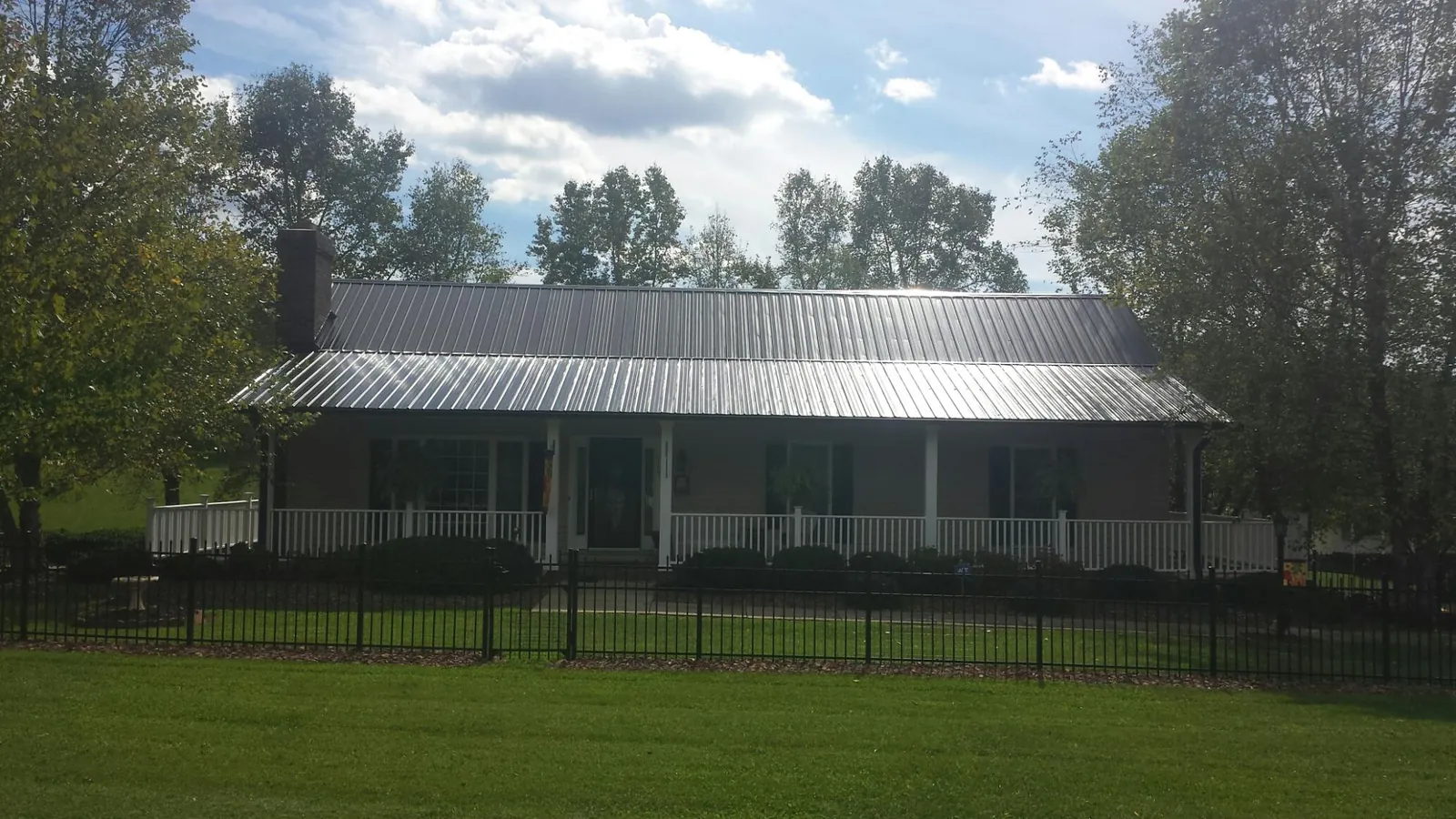 Gray metal roof on a brick ranch with a full width front porch — Gutter Guard Installation work by our crew in Spicer