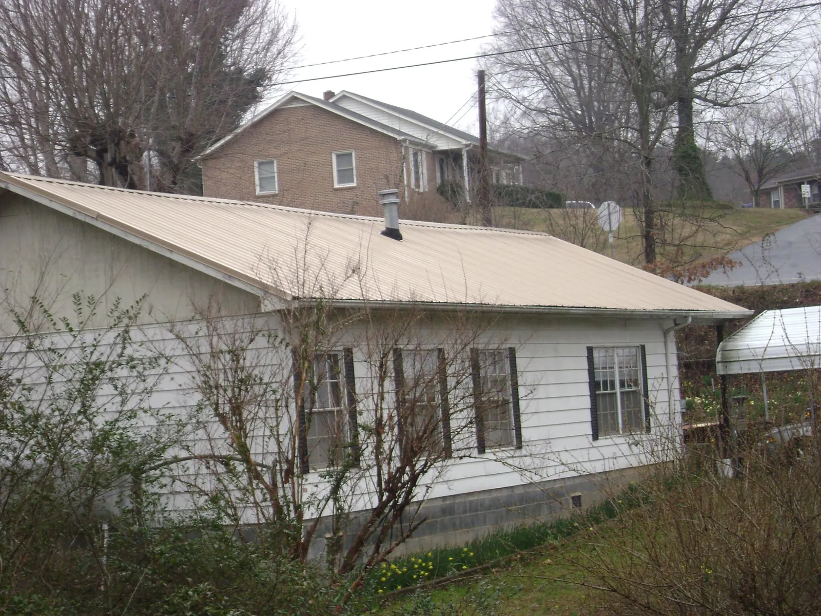 Tan metal roof on a white sided house set into a hillside — Commercial Roofing by Roofing Brothers in Spicer