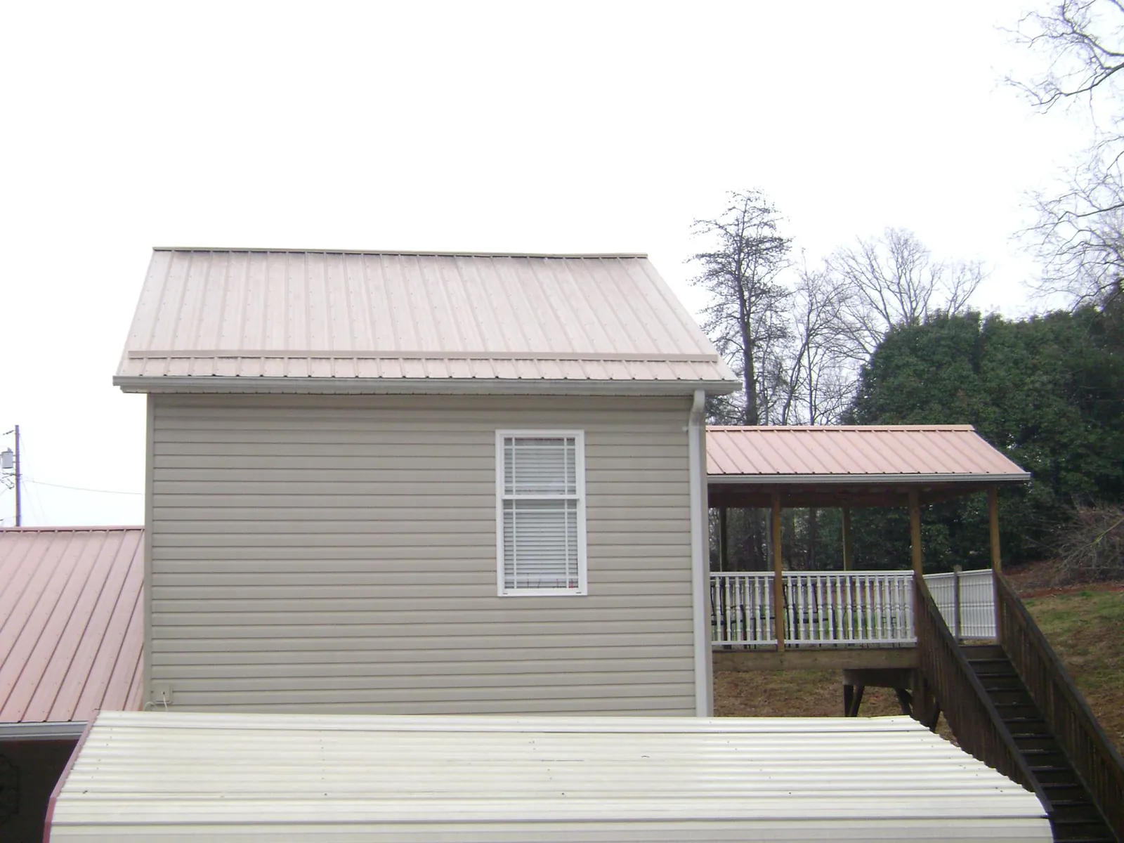 Tan metal roofs on a two story addition and attached porch, from a Roof Replacement job in Spicer